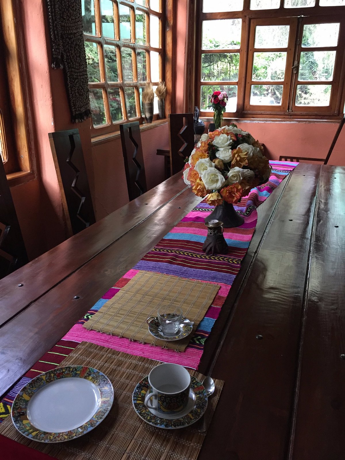 Traditional Ethiopian dining room with warm pink walls, wooden table set with colorful textiles, fresh floral centerpiece, and traditional coffee service creating an authentic hospitality experience